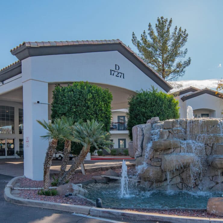 A welcoming entrance features a charming fountain surrounded by lush greenery, promoting community and comfort.